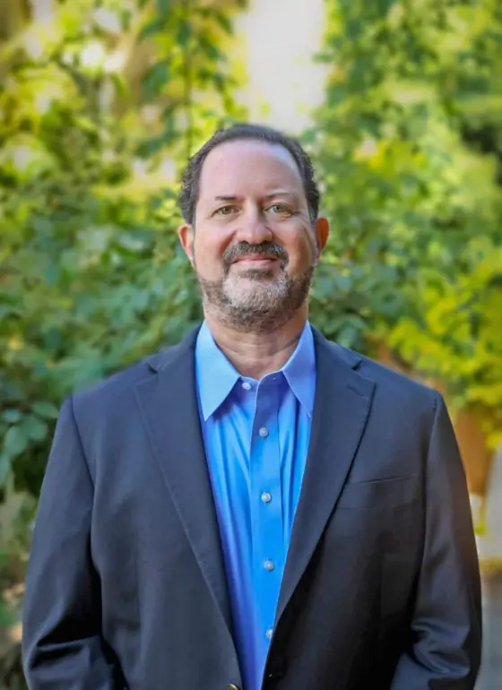 Man in suit jacket standing outdoors smiling